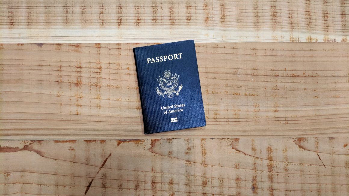 United States Passport book on plain light brown wooden surface.