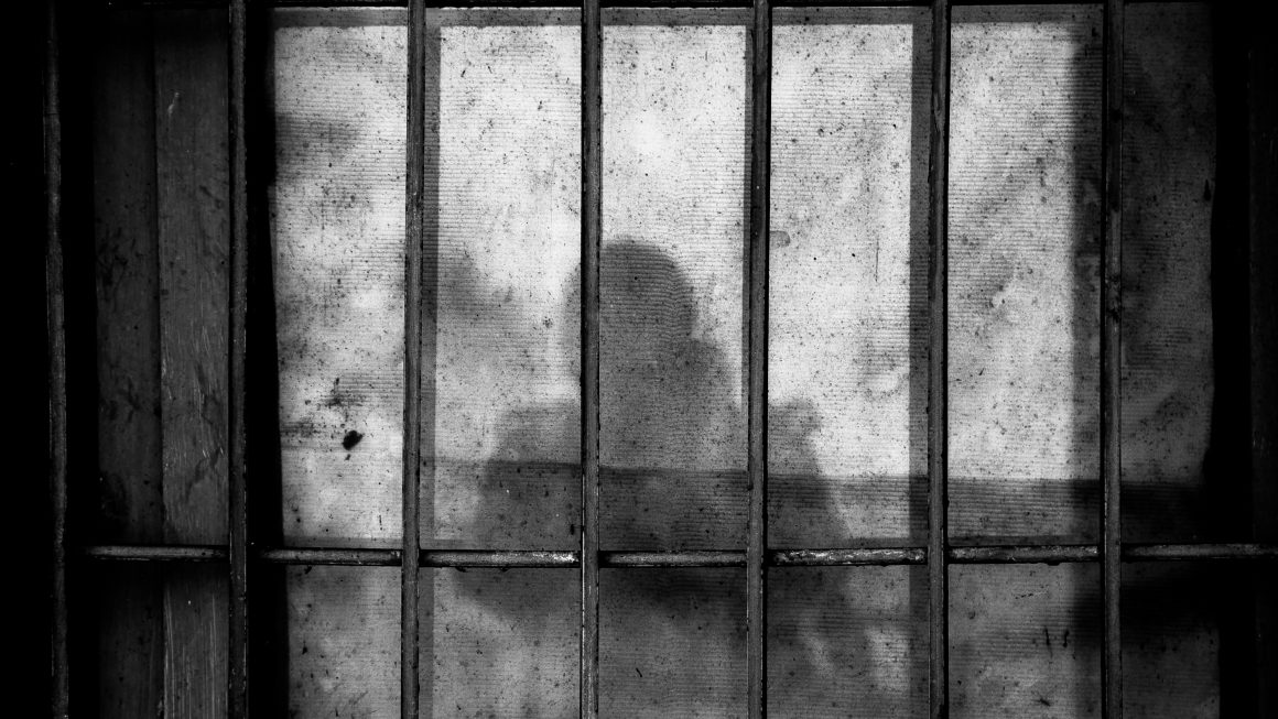 Shadow of person behind prison bars on concrete wall and ground