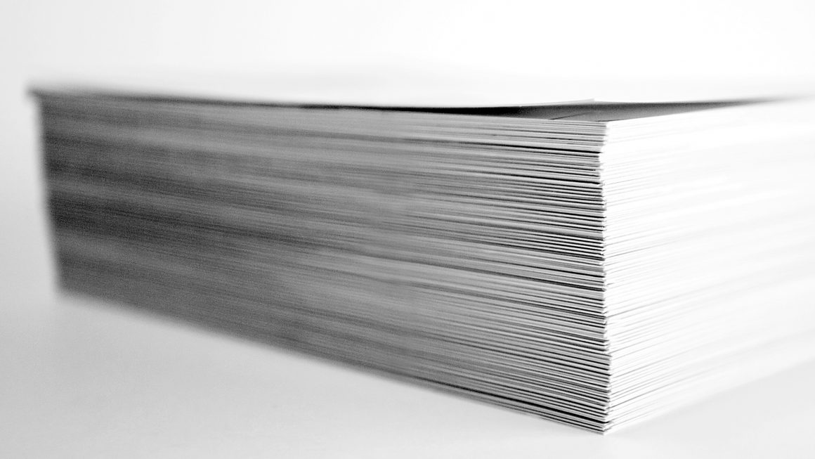 Tall stack of paper on top of a flat surface with plain background