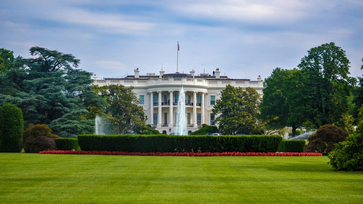 United States White House, front lawn, garden and fountain in front of blue sky.